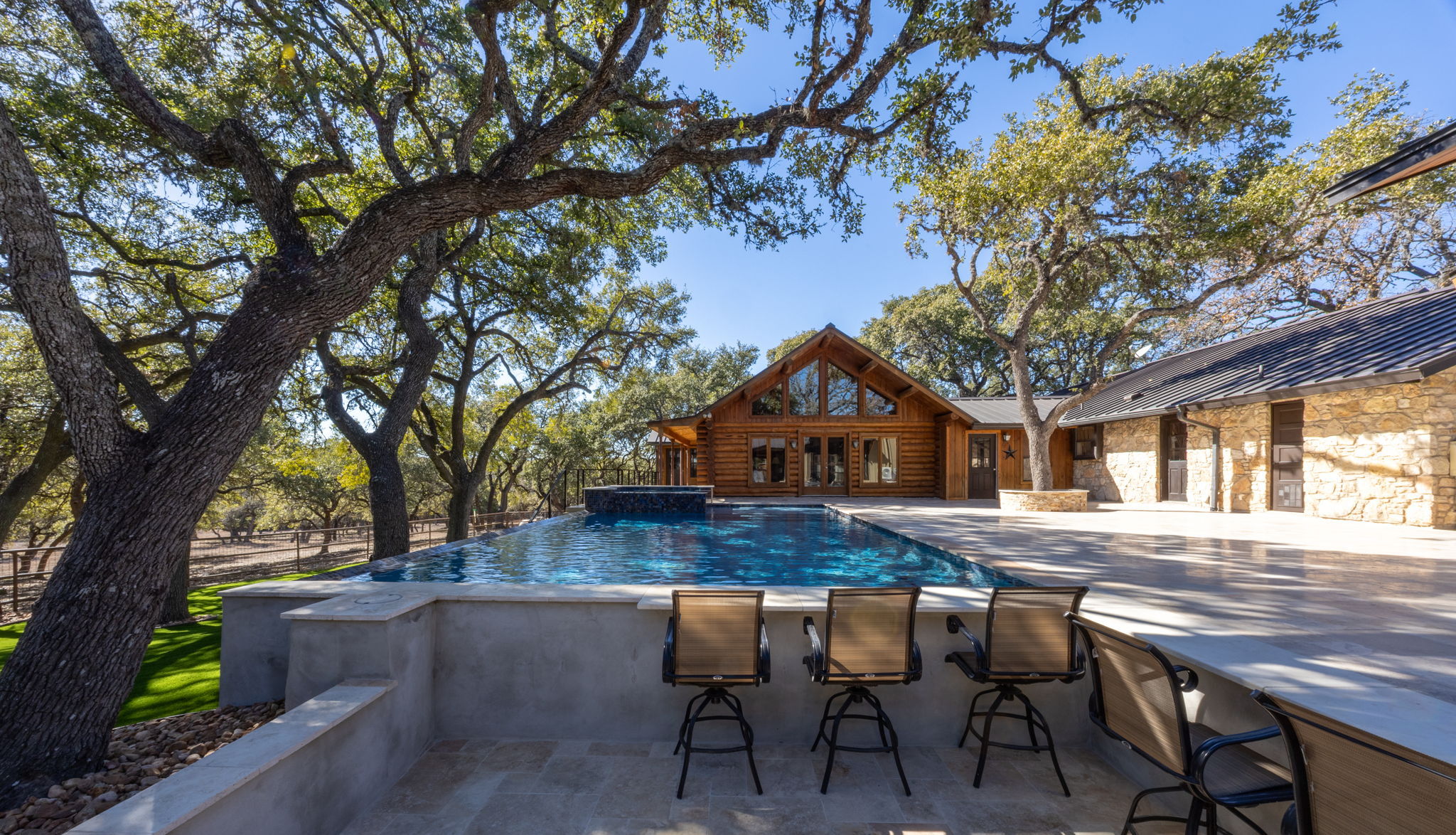 Geometric pool with integrated spa and sunken poolside bar set in an expansive stone patio framed by mature oak trees